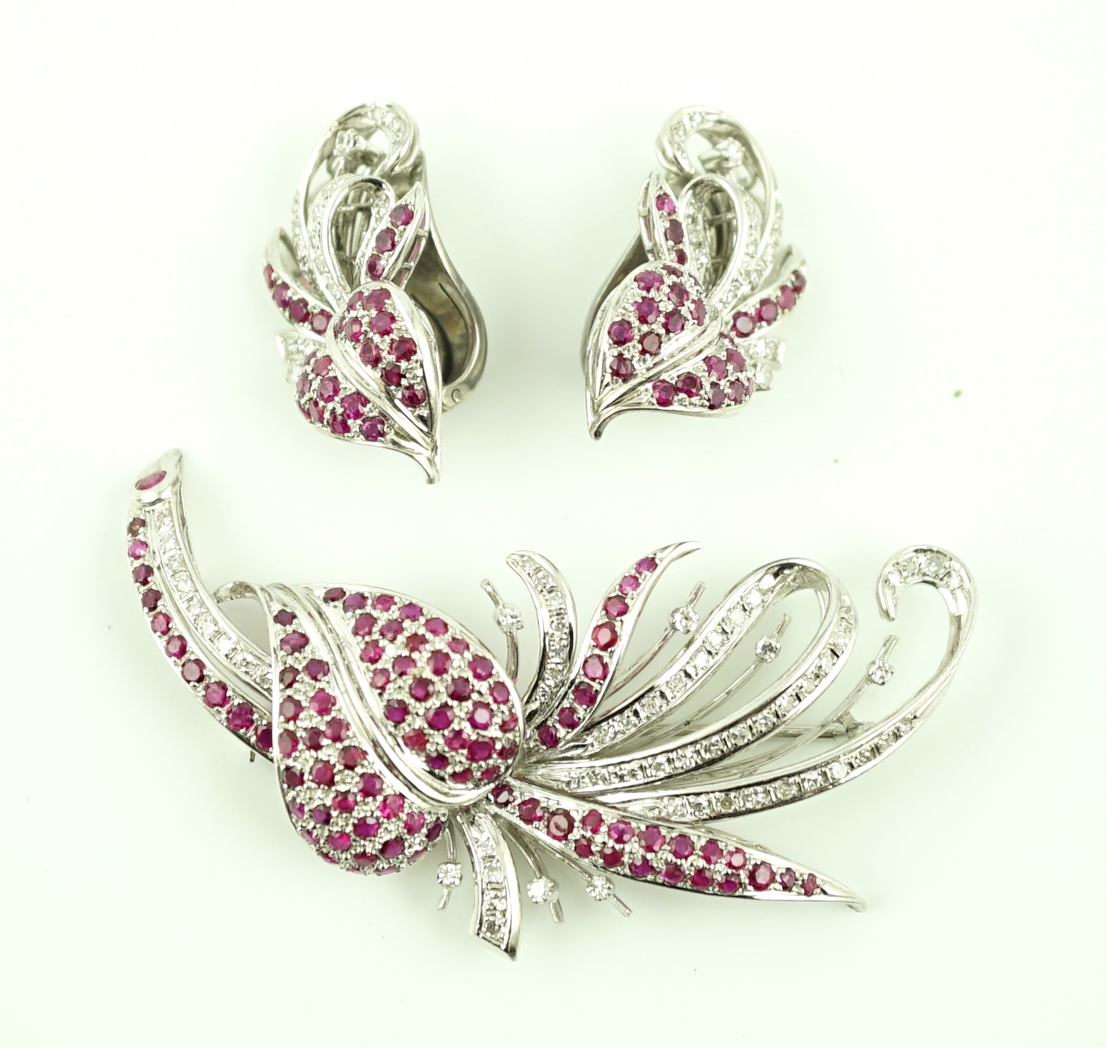 A suite of platinum?, diamond and ruby set cluster jewellery, comprising a spray brooch and pair of matching ear clips